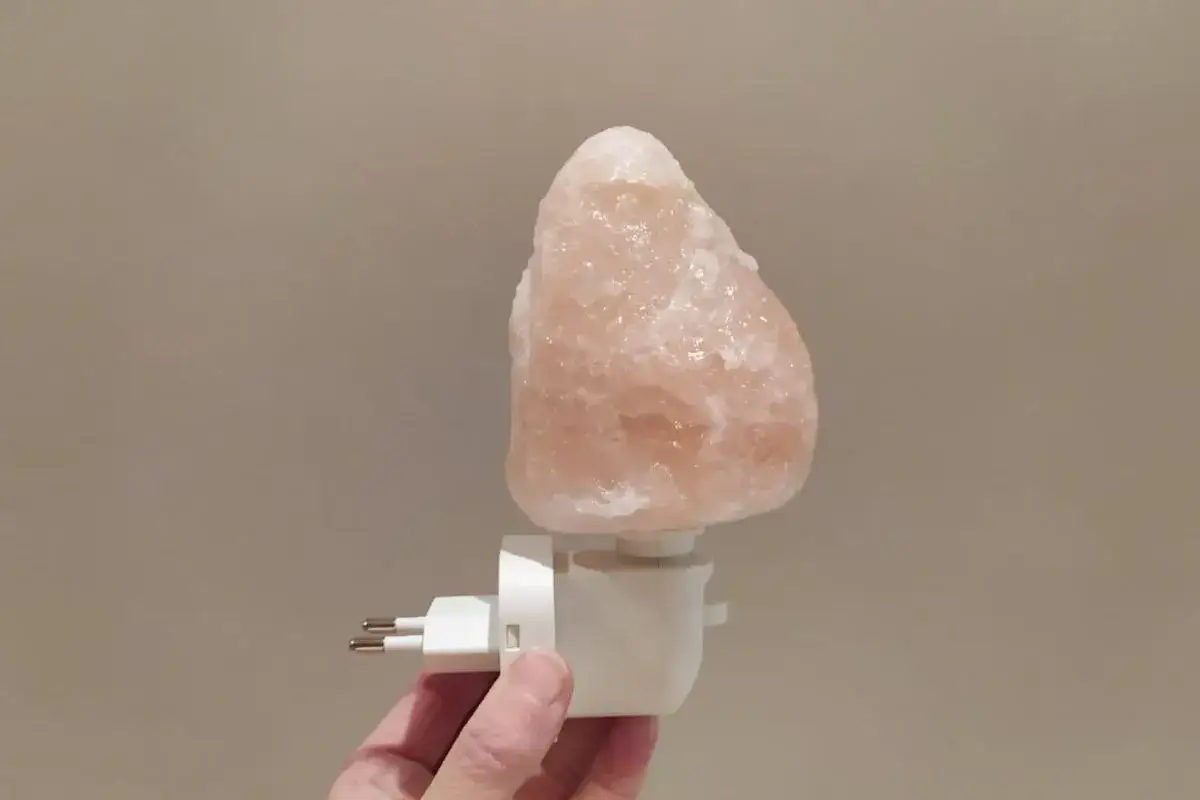 Una lámpara de sal rosa natural, con un enchufe blanco para la pared.