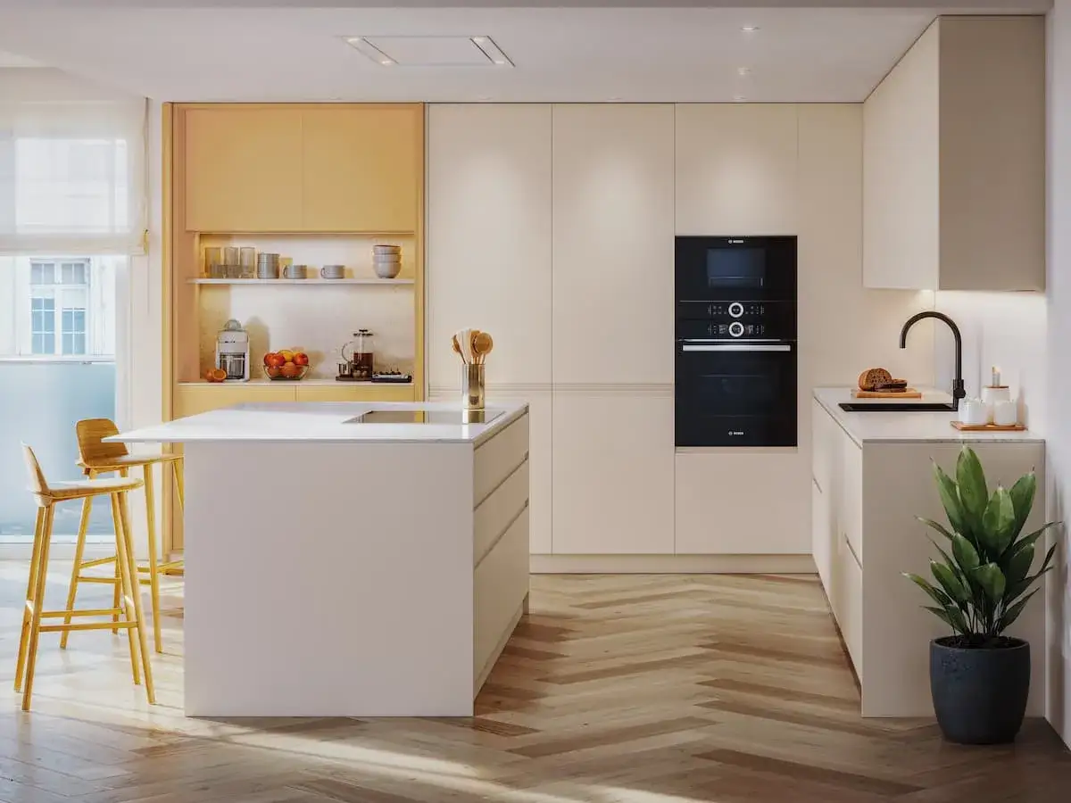 Cocina moderna con isla central y taburetes. Los colores de muebles de cocina son neutros, destacando el contraste con los armarios superiores amarillos.