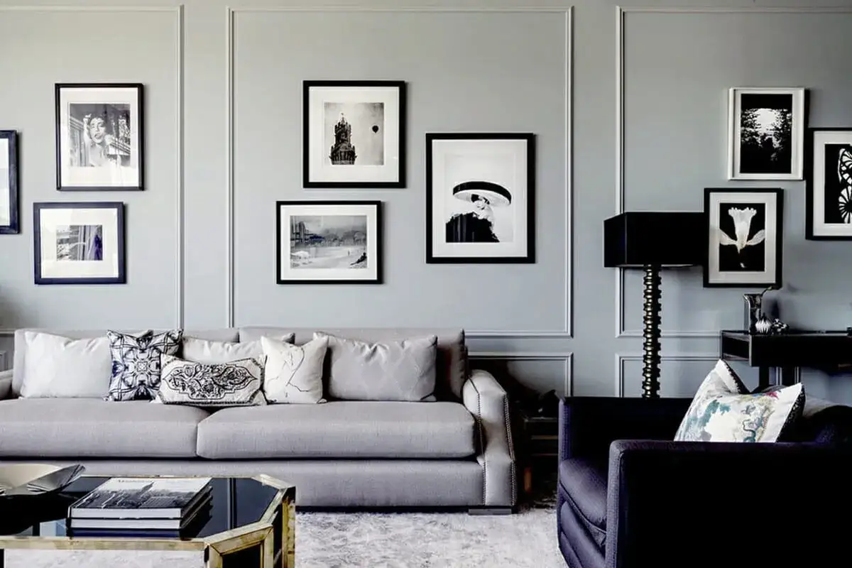 Elegante sal&oacute;n con sof&aacute; gris y varios cuadros en blanco y negro colgados en la pared, mostrando c&oacute;mo combinar cuadros en la pared con diferentes tama&ntilde;os y motivos.