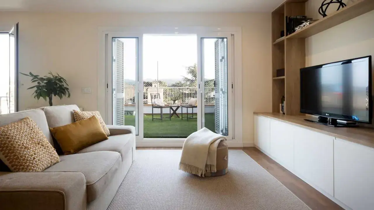 Sofá beige, alfombra gris y mueble de TV de madera. Un balcón con césped artificial y mobiliario exterior inspira un moderno diseño de interiores.