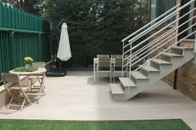 Escaleras exteriores casas de campo, con mesa y sillas de madera, sombrilla y valla verde.