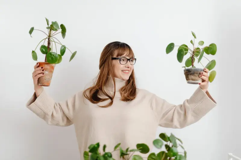 Mujer sonriente con gafas sostiene dos plantas altas de interior.