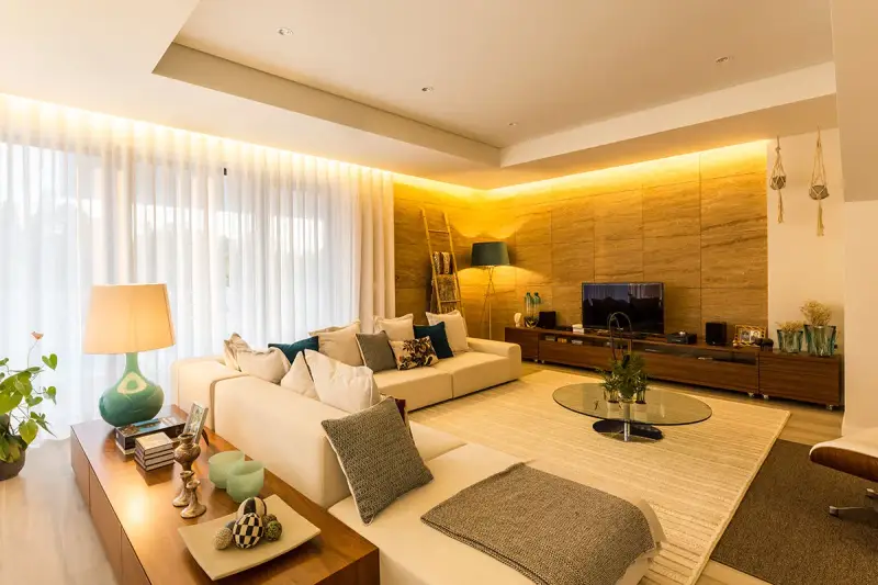Salón moderno con sofá blanco, mesa de centro de cristal y **iluminación indirecta** cálida que realza la pared de piedra.