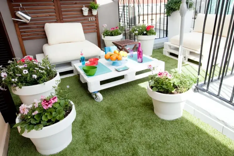 Balcón acogedor con césped artificial, muebles de palets y macetas con flores. ¡Ideas para terrazas con césped artificial!