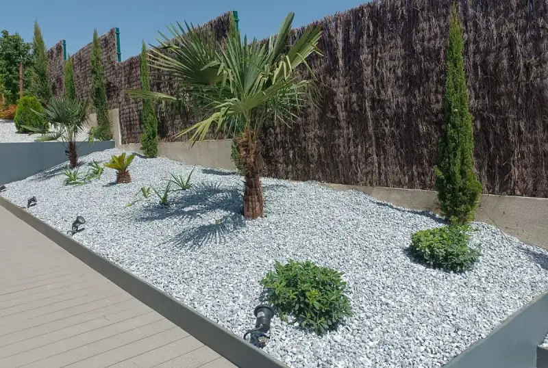Jardines con piedras blancas y plantas exóticas, como palmeras y cipreses, crean un oasis moderno.
